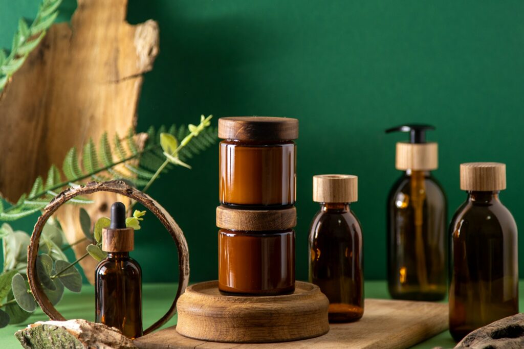 Glass brown containers for cosmetics with wooden lids. Cream, dropper bottle and lotion. Green back